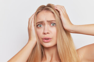 Naklejka premium Portrait of frightened blonde girl over background holding both hands on her head in fear, hard moment concept, copy space