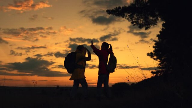 People resting in nature. Women tourists with backpacks travel in forest, raise their hands enjoy sunset sky. Slow motion. Working as team of two friends, young female travelers adventures on vacation