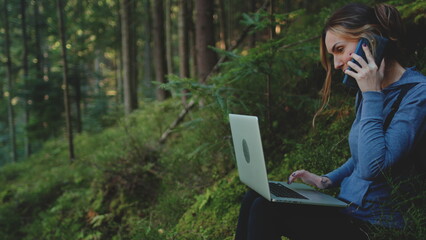 A woman working outdoors. Girl typing on laptop and talking by phone sitting in a green forest...