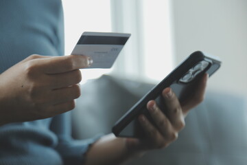 A credit card in the hands of a young businesswoman pays for a business on a mobile phone and on a desk with a laptop.