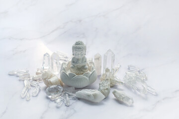 Clear quartz minerals and little Buddha statue on abstract light marble background. gemstones for Magic crystal ritual. esoteric spiritual practice for relaxation, meditation, life balance.