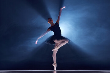 Elegance and grace in movements. Beautiful ballerina dancing over blue background with spotlight. Concept of classical dance, art and grace, beauty, choreography, inspiration