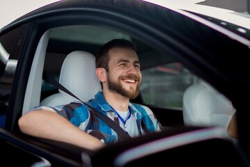 Smiling male passenger using safety belt, looking at the window while sitting in the car. Travel, lifestyle, transport concept