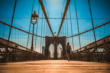 Girl strolls along the Brooklyn Bridge in New York City at sunset.