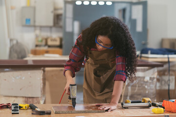 African American female carpenter working with pneumatic nail gun shoot to timber at wood factory....
