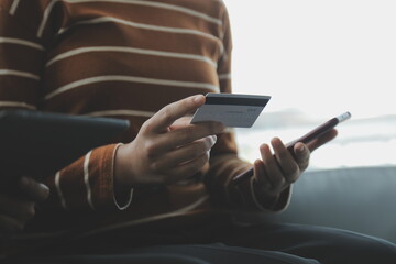 A credit card in the hands of a young businesswoman pays for a business on a mobile phone and on a desk with a laptop.