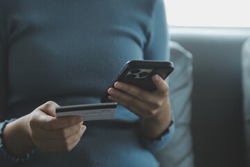 A credit card in the hands of a young businesswoman pays for a business on a mobile phone and on a desk with a laptop.