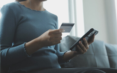 A credit card in the hands of a young businesswoman pays for a business on a mobile phone and on a desk with a laptop.