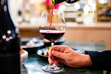 Waiter pouring red wine in glasses for wine on the table in restaurant