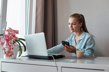 A young woman using a laptop communicates over the Internet with a client from the living room. Cozy workplace, remote work, e-learning concept