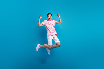 Fototapeta na wymiar Full body portrait of crazy energetic young man jumping raise fists accomplishment isolated on blue color background