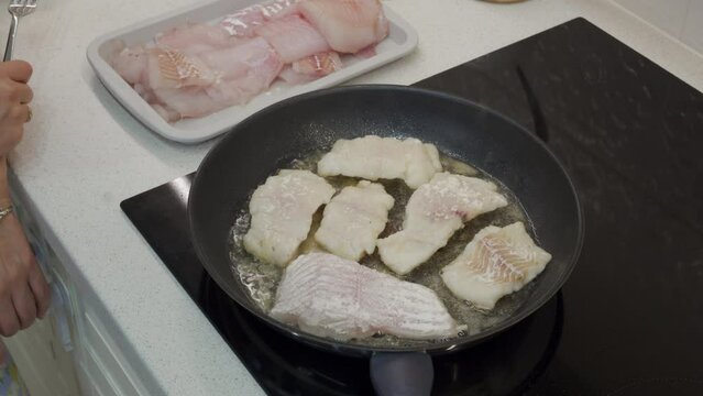 woman frying cod fish in a frying pan in the kitchen at home