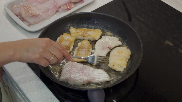 woman frying cod fish in a frying pan in the kitchen at home