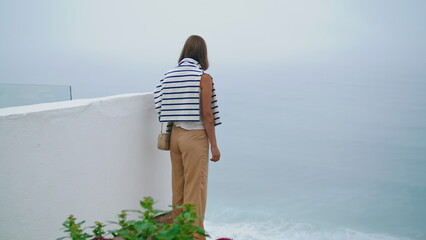 Girl looking seaside view on cliff top. Summer tourist admiring ocean landscape