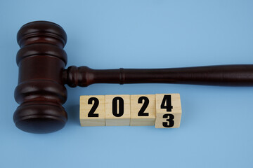 Judge gavel and numbers 2023 and 2024 on wooden cubes on blue background. Concept of new laws in year 2024.