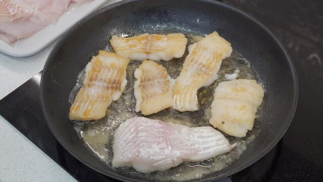 woman frying cod fish in a frying pan in the kitchen at home