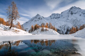 Autumnal landscape view of the Lac Bleu in Arolla with golden larches and snow-covered mountains - obrazy, fototapety, plakaty