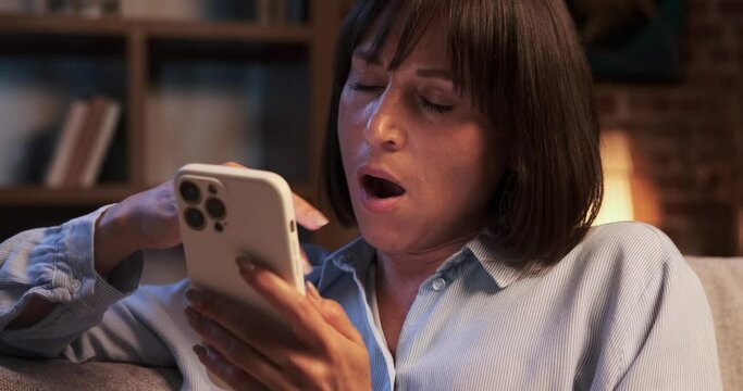 Bored woman sits with phone in hand, seeking solace in the digital world. Her eyes reflect a sense of ennui as she scrolls through device, searching for something captivating.