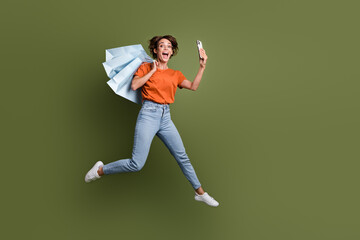 Full length photo of excited girl in stylish clothes doing selfie on smartphone jump with new outfit isolated on green color background