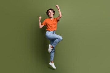 Fototapeta na wymiar Full length photo of ecstatic girl wear stylish clothes jumping raising fists scream yes win bet isolated on green color background