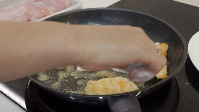 woman frying cod fish in a frying pan in the kitchen at home