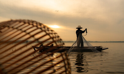 Silhouette of fisherman at sunrise, Standing aboard a rowing boat and casting a net to catch fish for food - obrazy, fototapety, plakaty