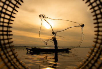 Silhouette of fisherman at sunrise, Standing aboard a rowing boat and casting a net to catch fish...