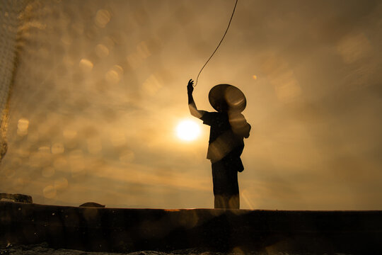 Silhouette of fisherman at sunrise, Standing aboard a rowing boat and casting a net to catch fish for food