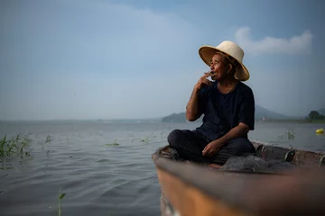 Foto op Canvas A fisherman relaxes in a boat on the lake while smoking. © Wosunan