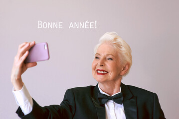 stylish mature senior woman in tuxedo with cellphone video calling or making selfie. Fun, party, style, lifestyle, business, technology, celebration concept