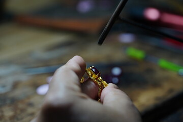 A goldsmith is installing gemstones into the ring to make it beautiful.