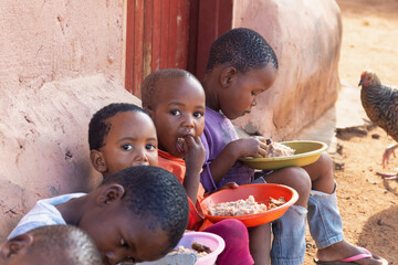 group of village african children eating in the yard, famine and malnutrition NGO solving world problems - obrazy, fototapety, plakaty