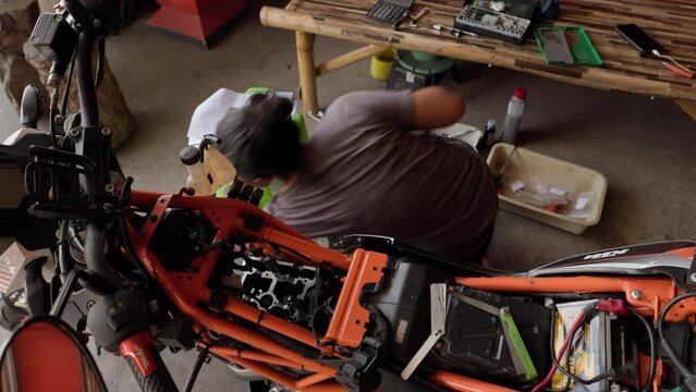 Repairing The Engine Of An Orange Motorcycle: 50 Year Old Asian Woman At Work