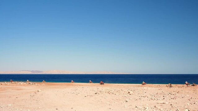 Wide view of group of tourists riding ATV bikes on the sandy beach of the Red Sea. Excursion to the desert in Dahab, Egypt
