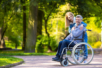Man on a wheelchair having a walk in the park with his wife