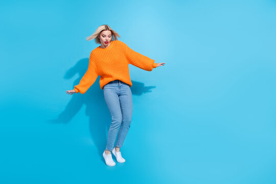 Full length photo of cute girl with blond hair wear knit orange jumper jeans look down empty space isolated on blue color background