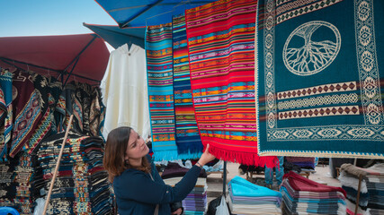 Beautiful young Latin American woman buying multicolored fabrics in the Plaza de los Ponchos in the...