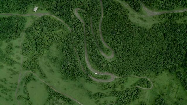 Winding mountain road between dense green forest near Gnevank Monastery in Lori Armenia. There are cars going off on the highway. Drone video. The camera lowers down.