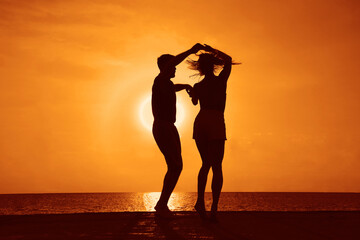 latin hispanic couple is dancing bachata above sea on summer beach. Sunset over water.Two silhouettes against the sun. Just married couple hugging. Romantic love story. Man and woman in holiday trip. - obrazy, fototapety, plakaty