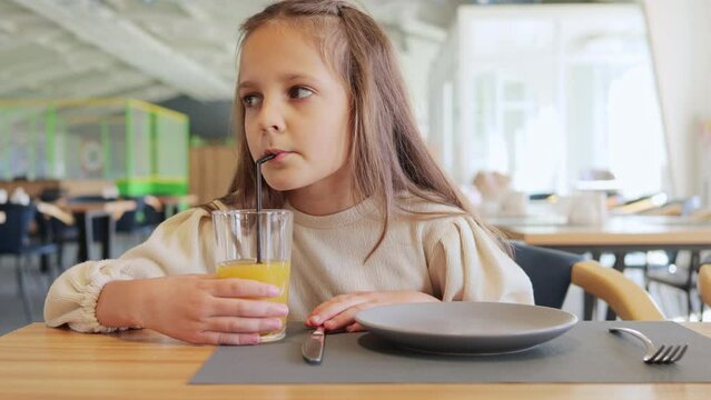 Girl child with brown drinking juice in cafe looking around having lunch in entertainment center enjoying fresh beverage.