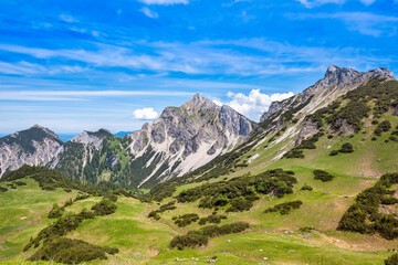 Fototapeta na wymiar Tannheimer Tal green grassy plain and mountain range against blue sky