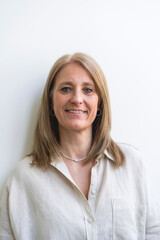Beautiful mid aged woman looking at camera leaning on white wall.