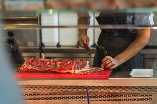 Un macellaio affetta una costosa bistecca dietro il banco di una macelleria.