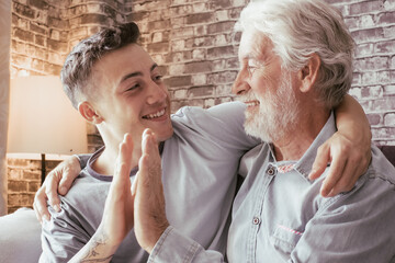 Young boy and his grandfather smile as they high five each other while sitting on the sofa at home, old and new generation - caring for the people we love