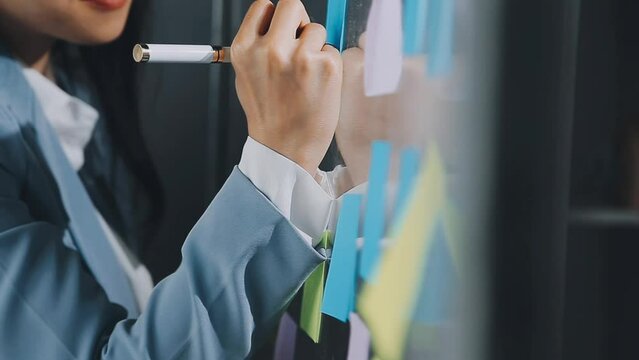 Young asian business woman working on project plan using sticky papers notes on glass wall, people meeting to share idea, Business design planning concepts.