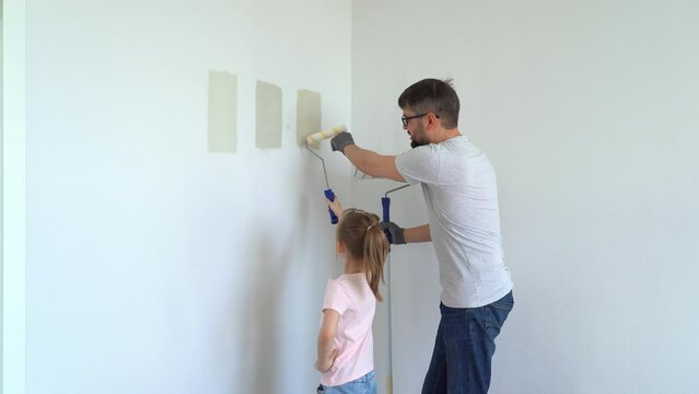 Happy family, father and little daughter choose wall paint on test of different colors at home in apartment. Repair concept, molar work