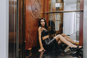 Photo, close-up portrait of a beautiful sexy young girl, brunette woman with curly hair, Armenian woman in black lingerie, leather dress in a retro hotel elevator.