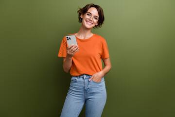 Portrait of toothy beaming nice person wear stylish t-shirt in eyewear hold smartphone arm in pocket isolated on green color background