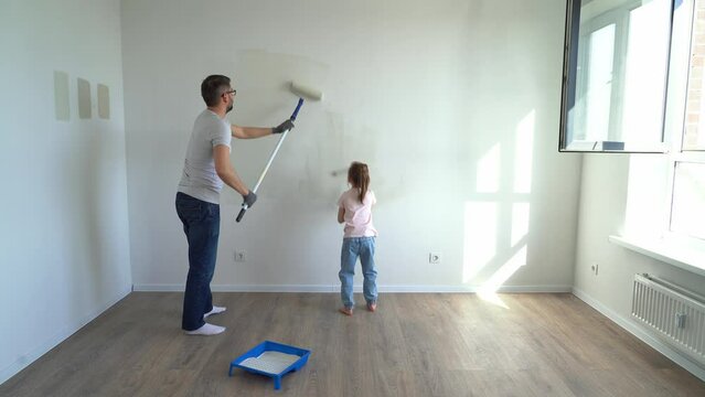 Back view father and little daughter paint wall with rollers at home in apartment. Family make renovations in new flat. Repair concept, molar work