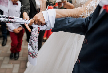 The bride and groom stand at the ceremony with an embroidered towel tied in a knot on their hands. Wedding photography, Ukrainian tradition, ritual, portrait, lifestyle. - obrazy, fototapety, plakaty